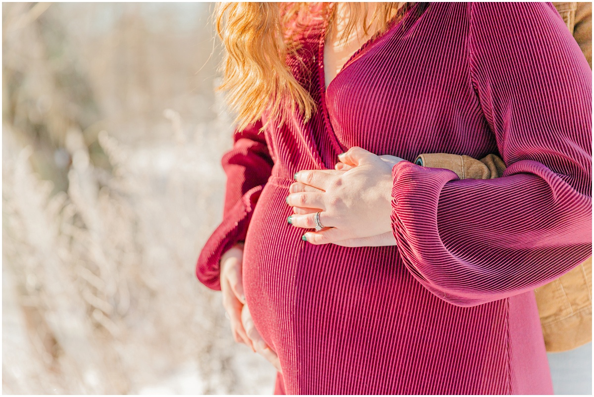 Mom and Dad's hands cradling bump in snowy maternity photo