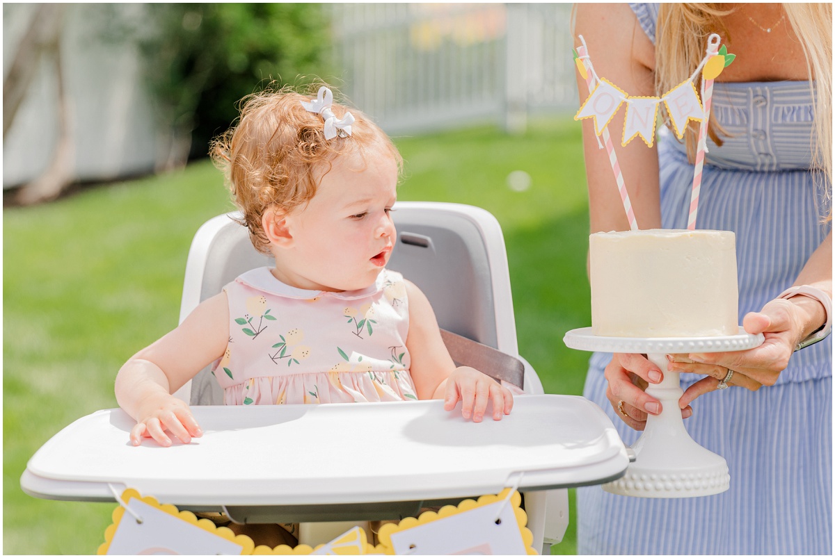 girl in high chair looking at smash cake