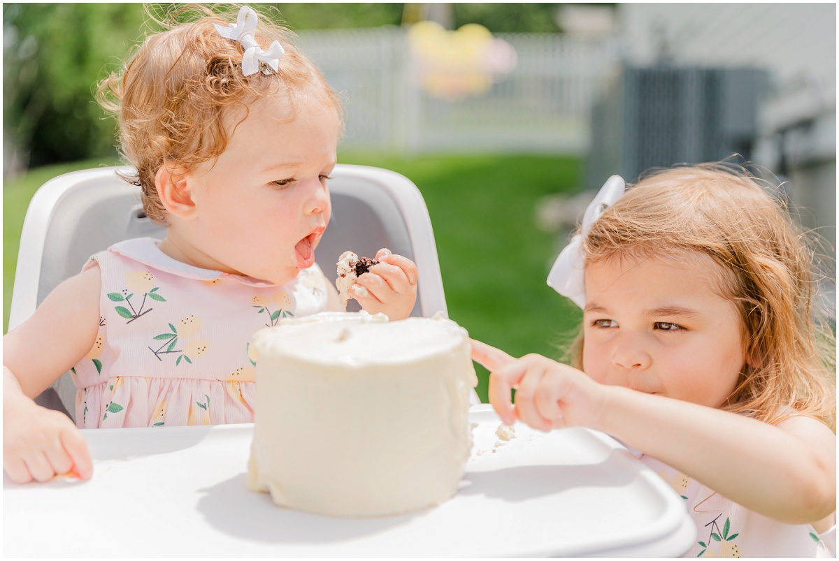 One-year-old in high chair and sister tasting smash cake frosting