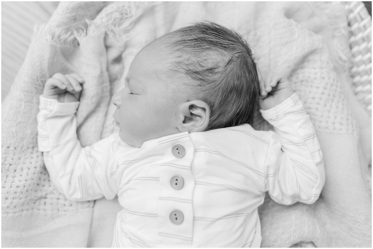 Black and white photo of sleeping baby's head turned to the left with his hands on either side of his head