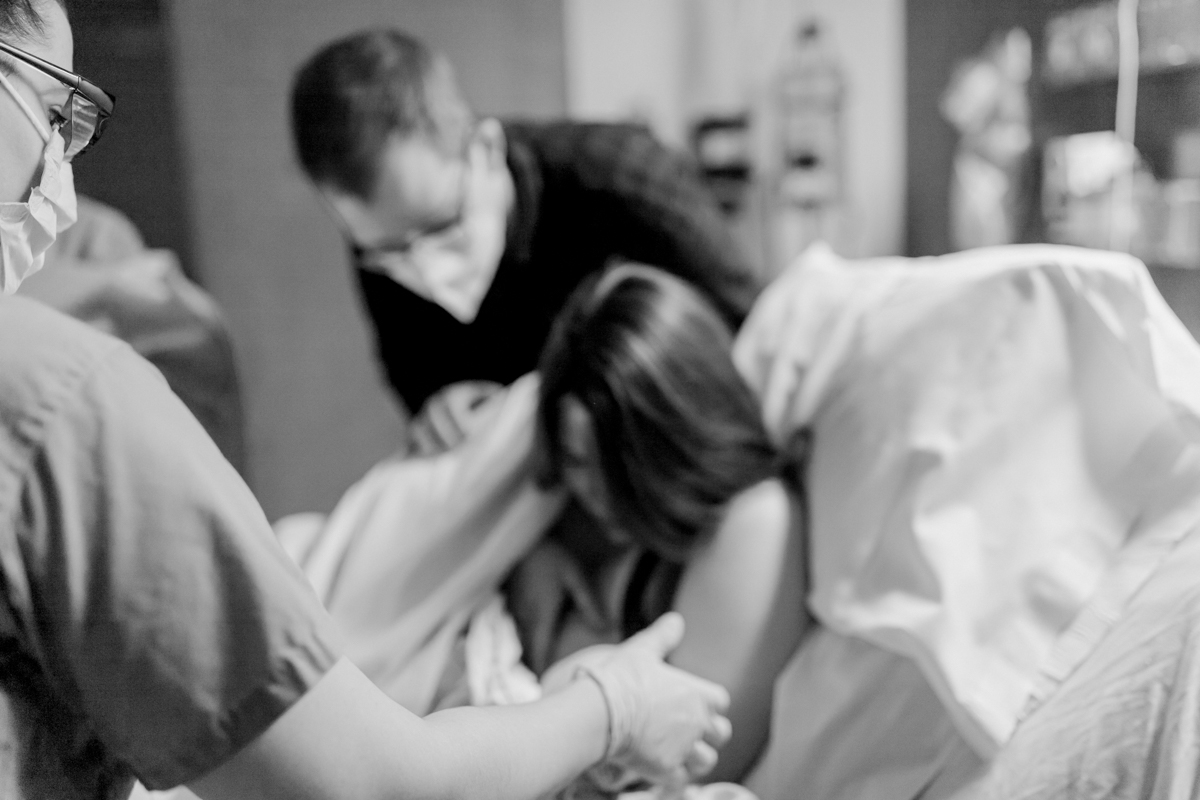 Black and white image shows midwife from AFA OBGYN Westford reaching out to mother who is holding just born baby to her chest while father looks on over her shoulder