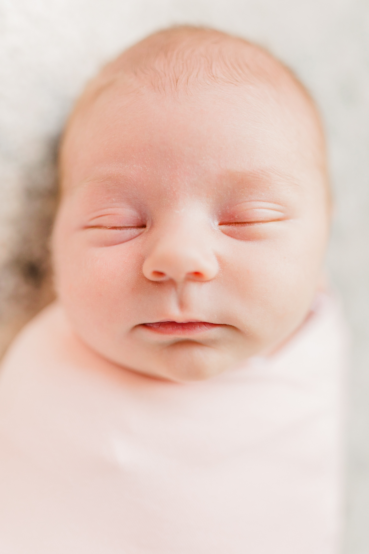 Boston Fertility Clinics | Close up of the face of a sleeping baby wrapped tightly in a light pink swaddle