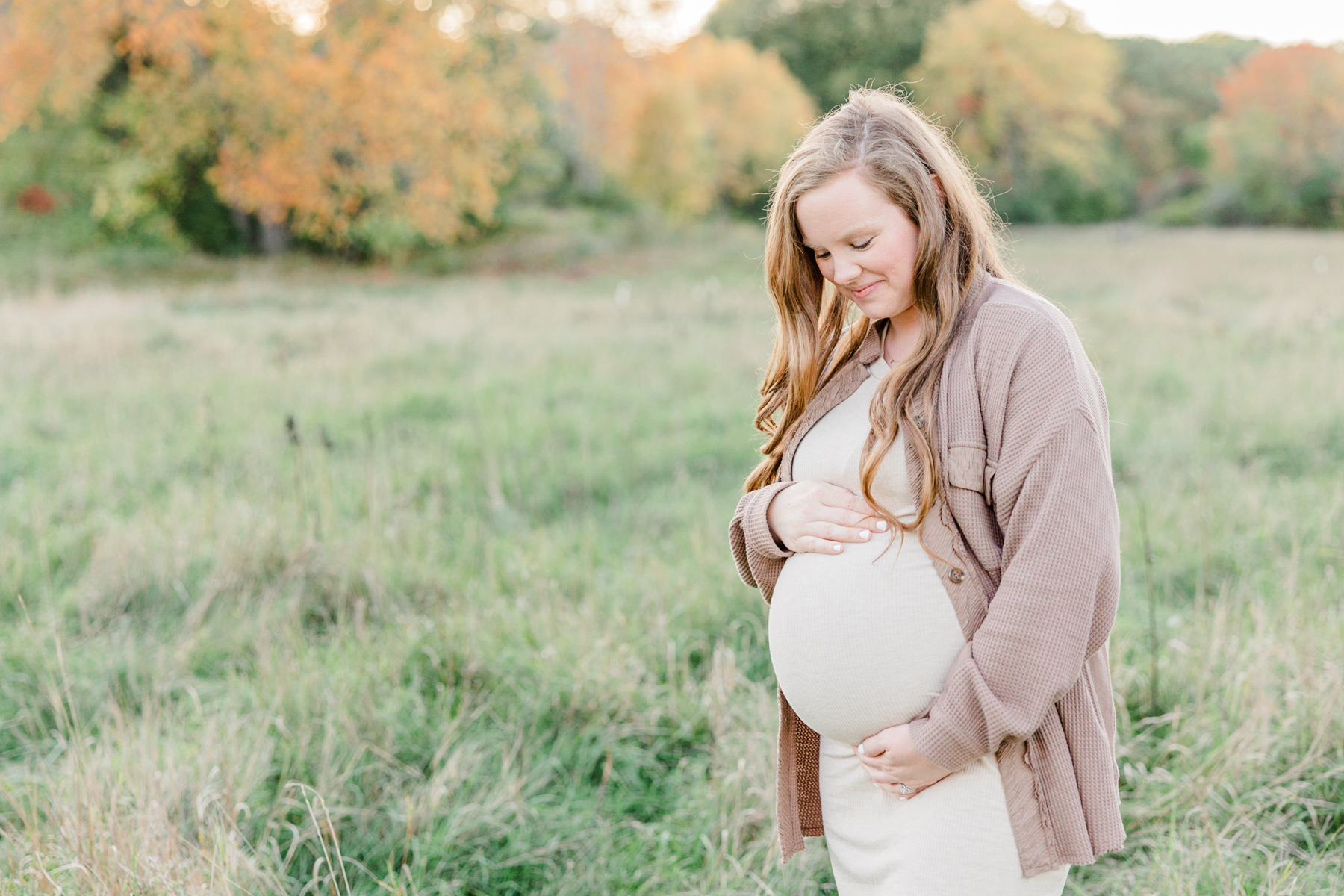 Pregnant client of Seven Sisters Midwifery standing in a field and smiling down at her bump