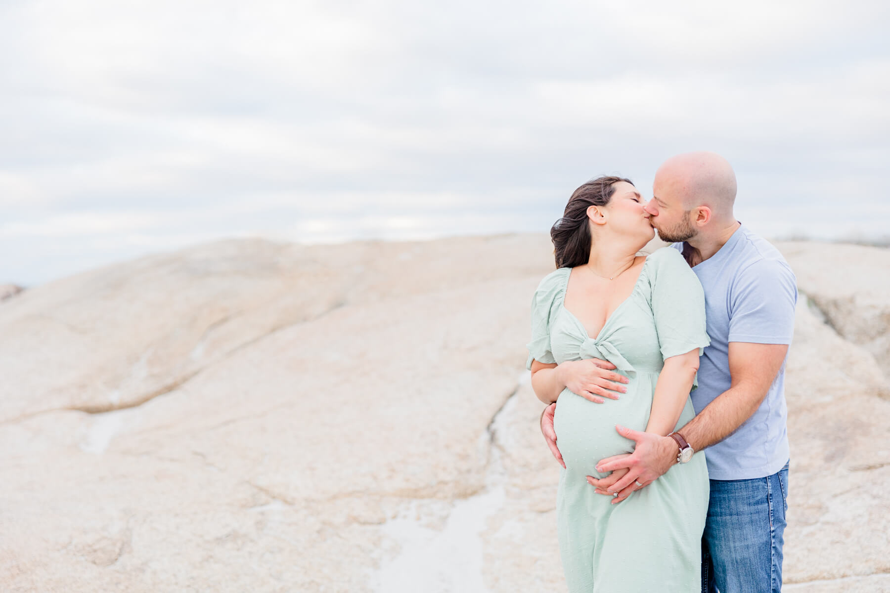 A mother to be and husband kiss while holding on the the bump
