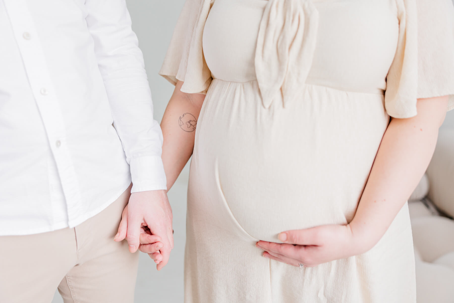 Details of a pregnant couple holding hands while standing in a studio