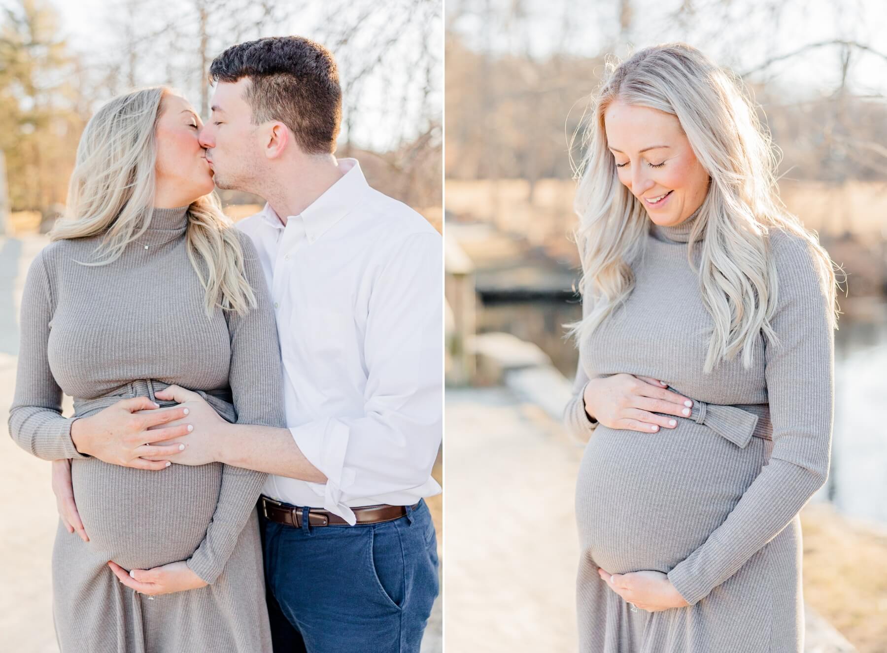 A mom to be and dad to be kiss while standing in a park on a river next to mom smiling down to her bump in a grey dress