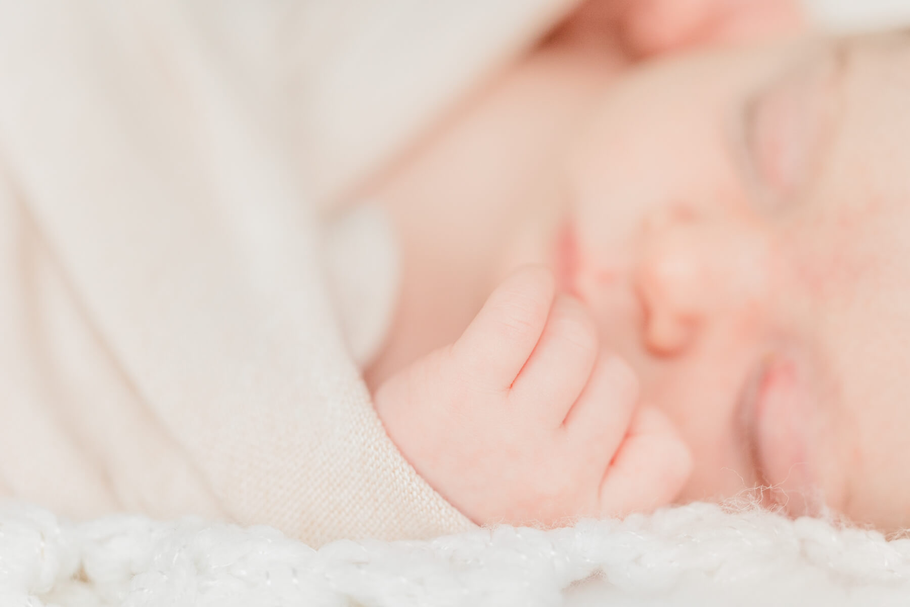 Details of a sleeping newborn baby's hand on a white bed and tan swaddle