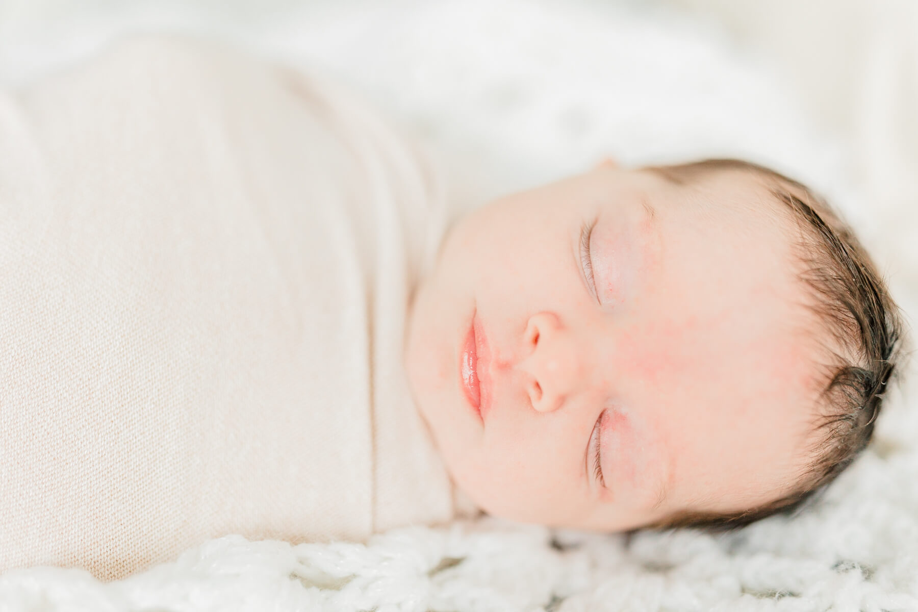 A newborn baby sleeps in a tan swaddle in a crib from nursery furniture Boston