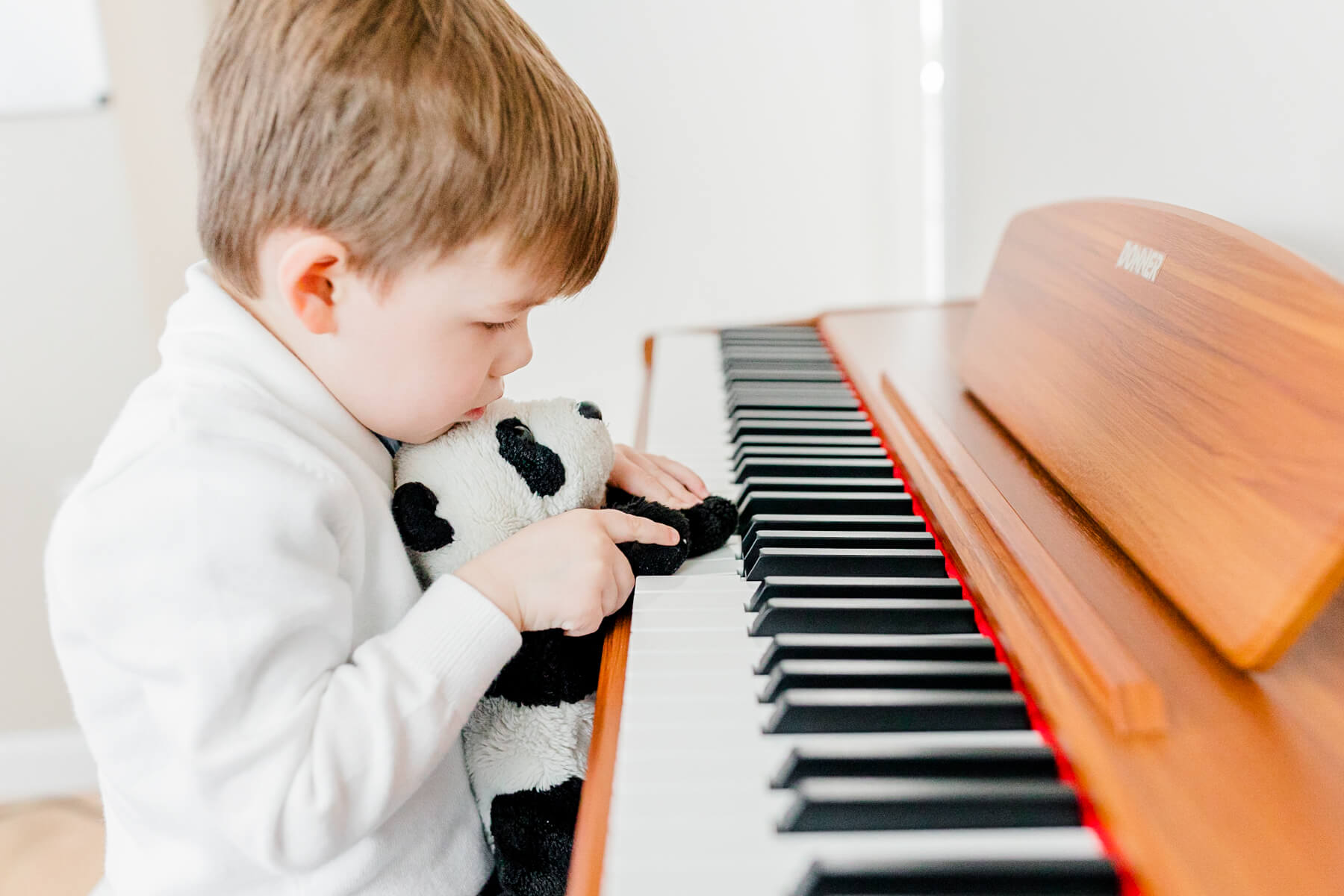 A young boy plays piano with the paws of a stuffed panda from boing toy shop