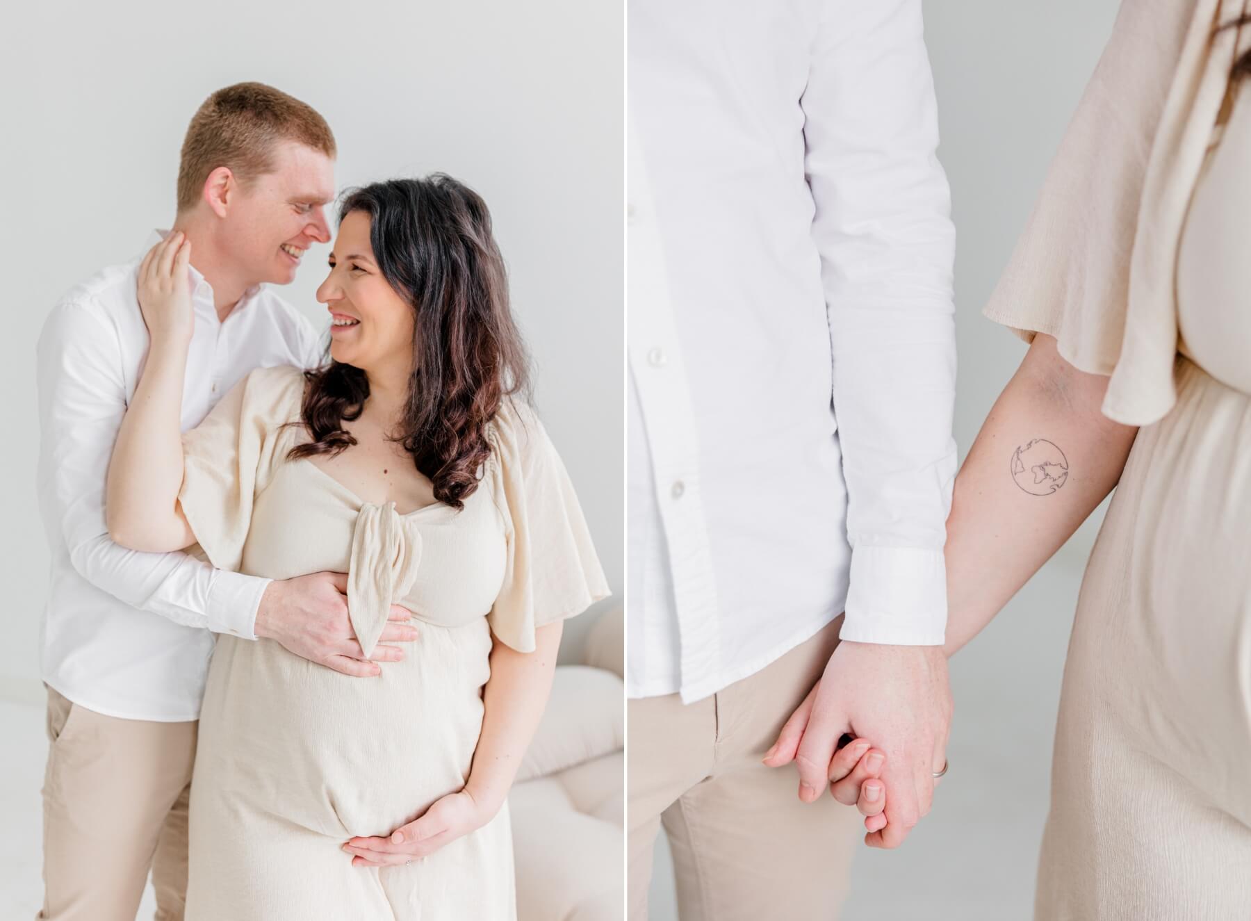 Expecting parents hold hands and share a laugh while standing in a studio in beige and white after visiting afa obgyn